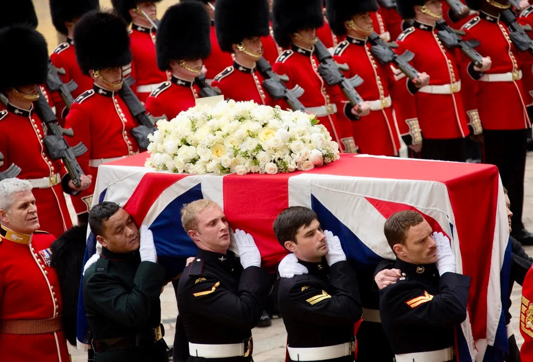 Flag-draped coffin at a ceremonial funeral procession with a classic white floral tribute, reflecting, by Pulbrook & Gould