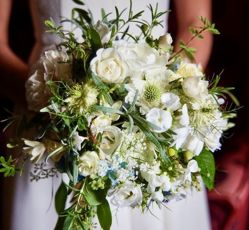White bridal bouquet with roses and foliage held by a bride