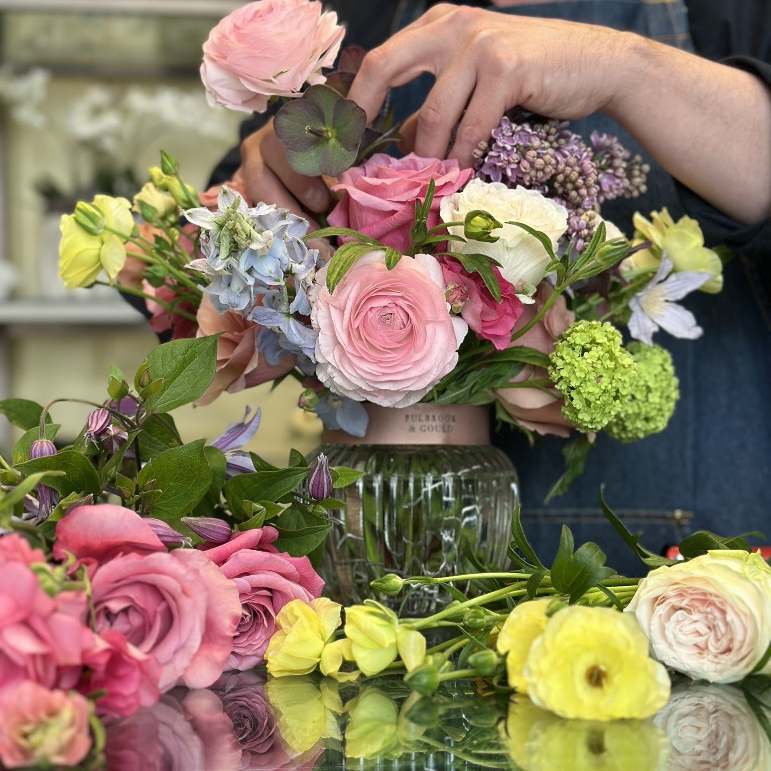 Hands arranging pink roses and spring flowers in a vase