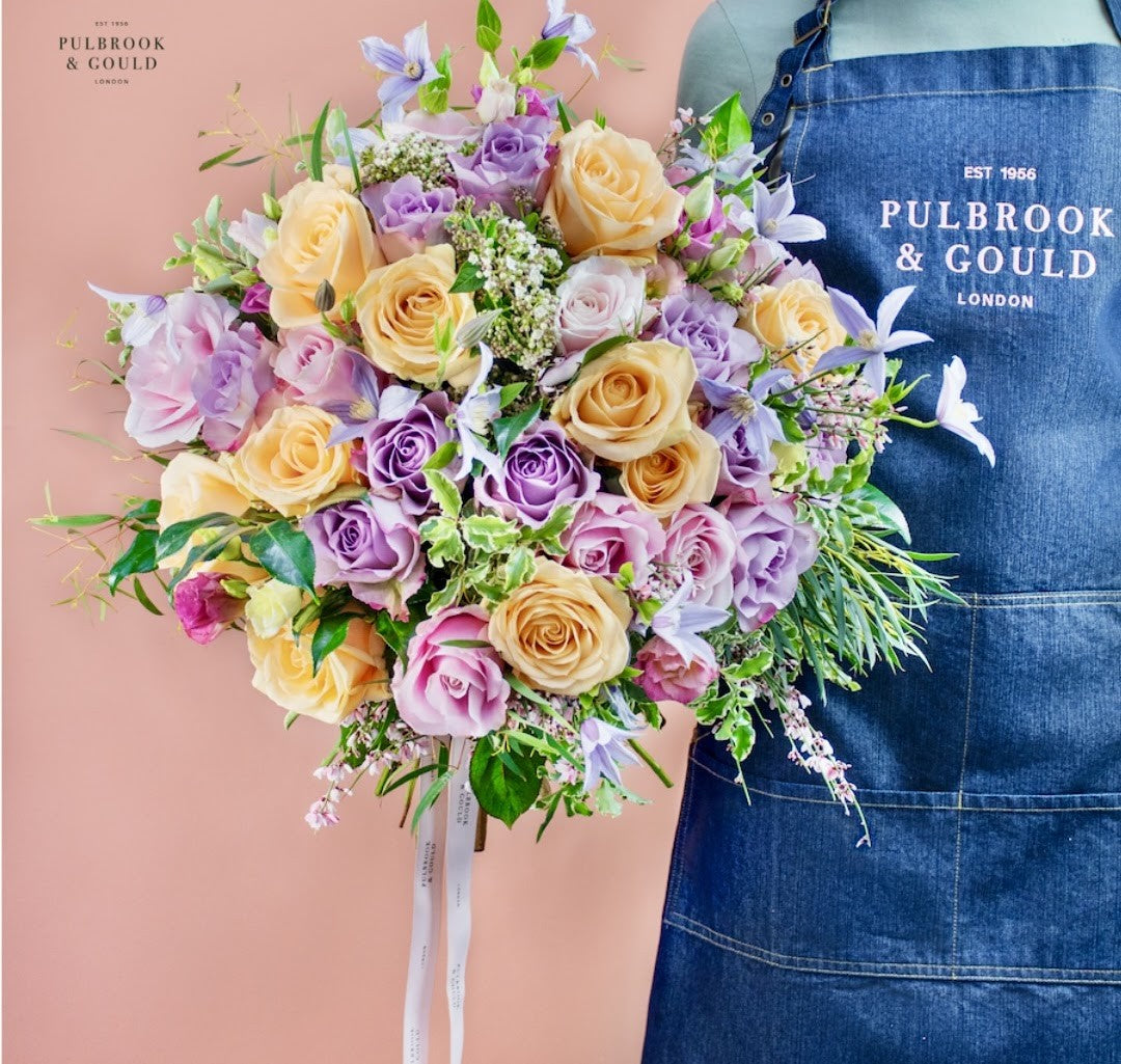 Peach and lilac rose hand-tied bouquet held beside a Pulbrook & Gould apron