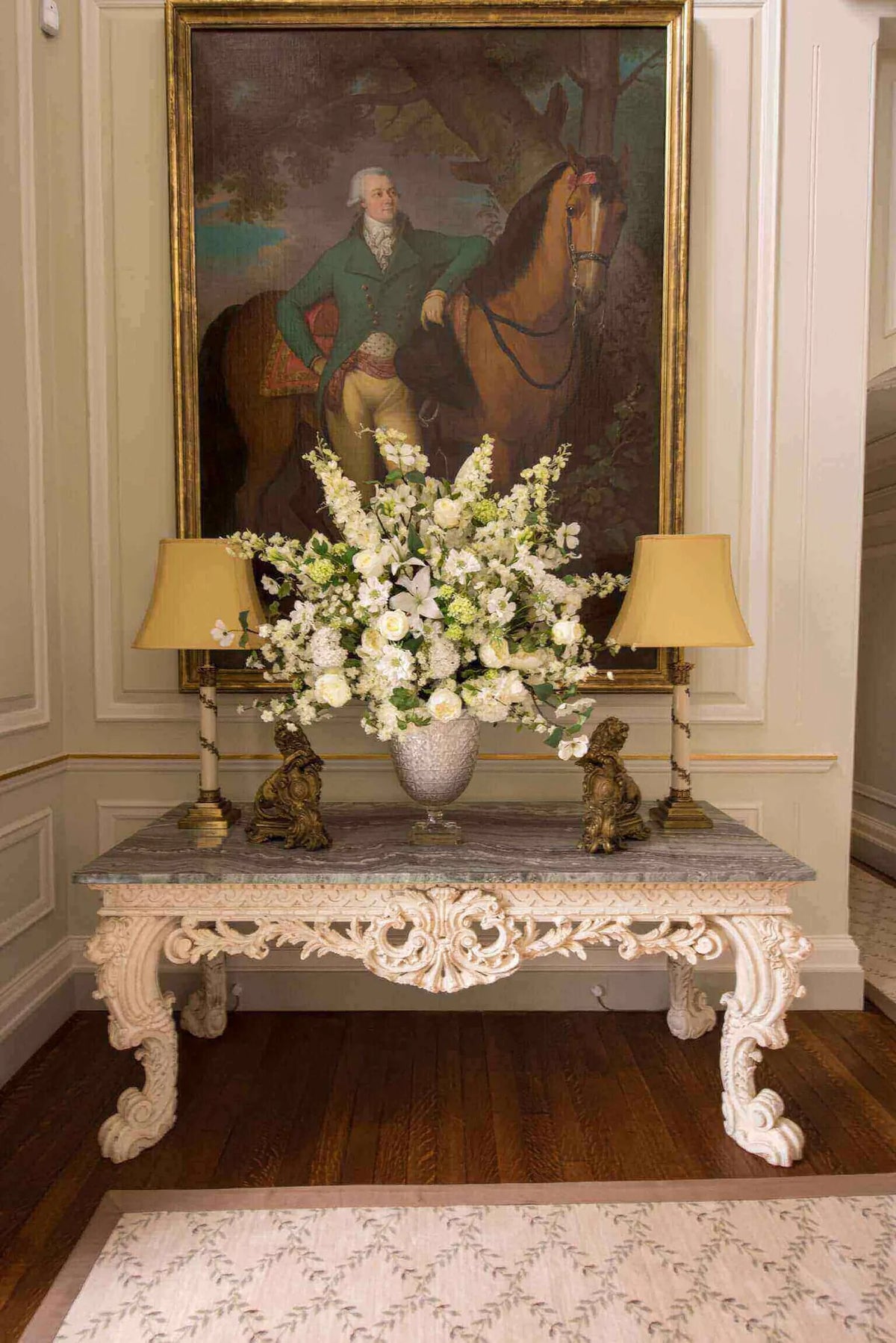 White flower arrangement on a console table beneath an equestrian portrait by Pulbrook & Gould