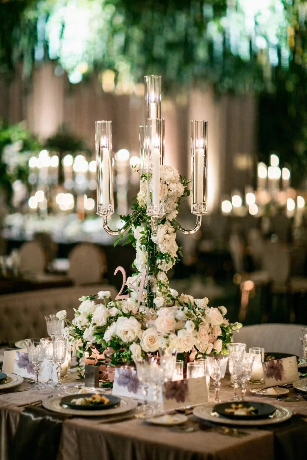 Luxury wedding tablescape with a tall glass candelabra, cascading white roses and foliage, and candlelit, by Pulbrook & Gould