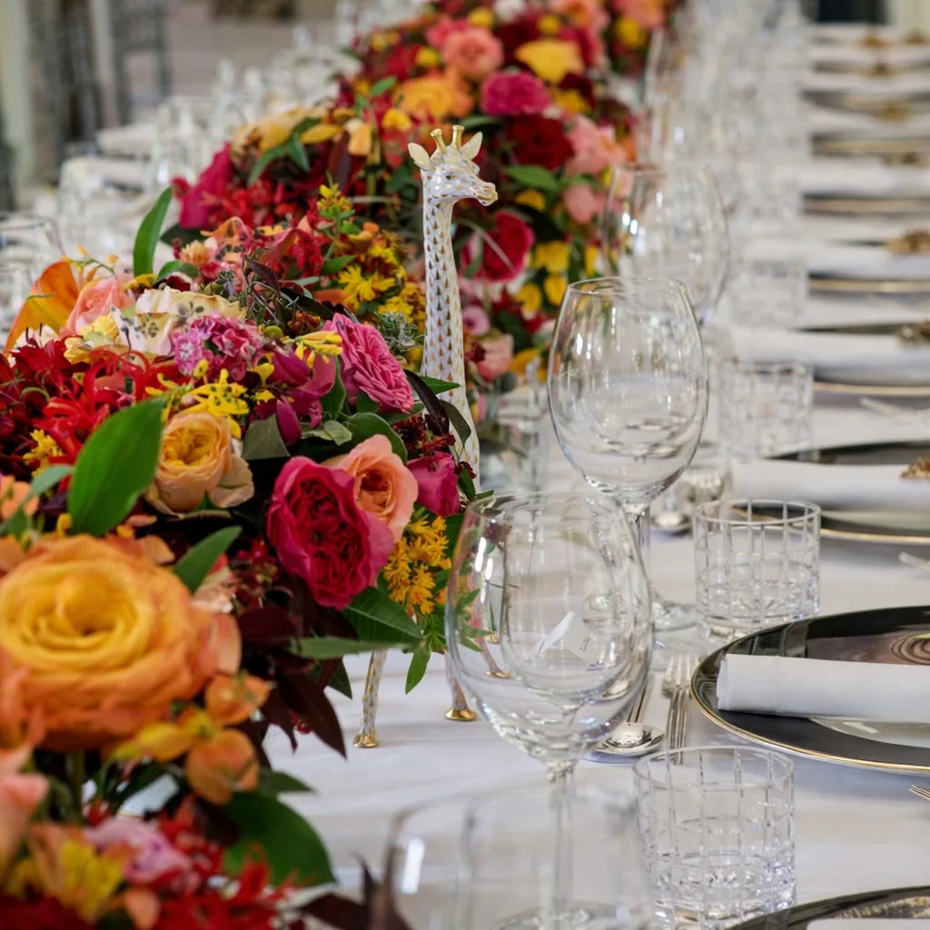 Vibrant long-table tablescape with jewel-coloured floral runner, decorative giraffe ornament and, by Pulbrook & Gould