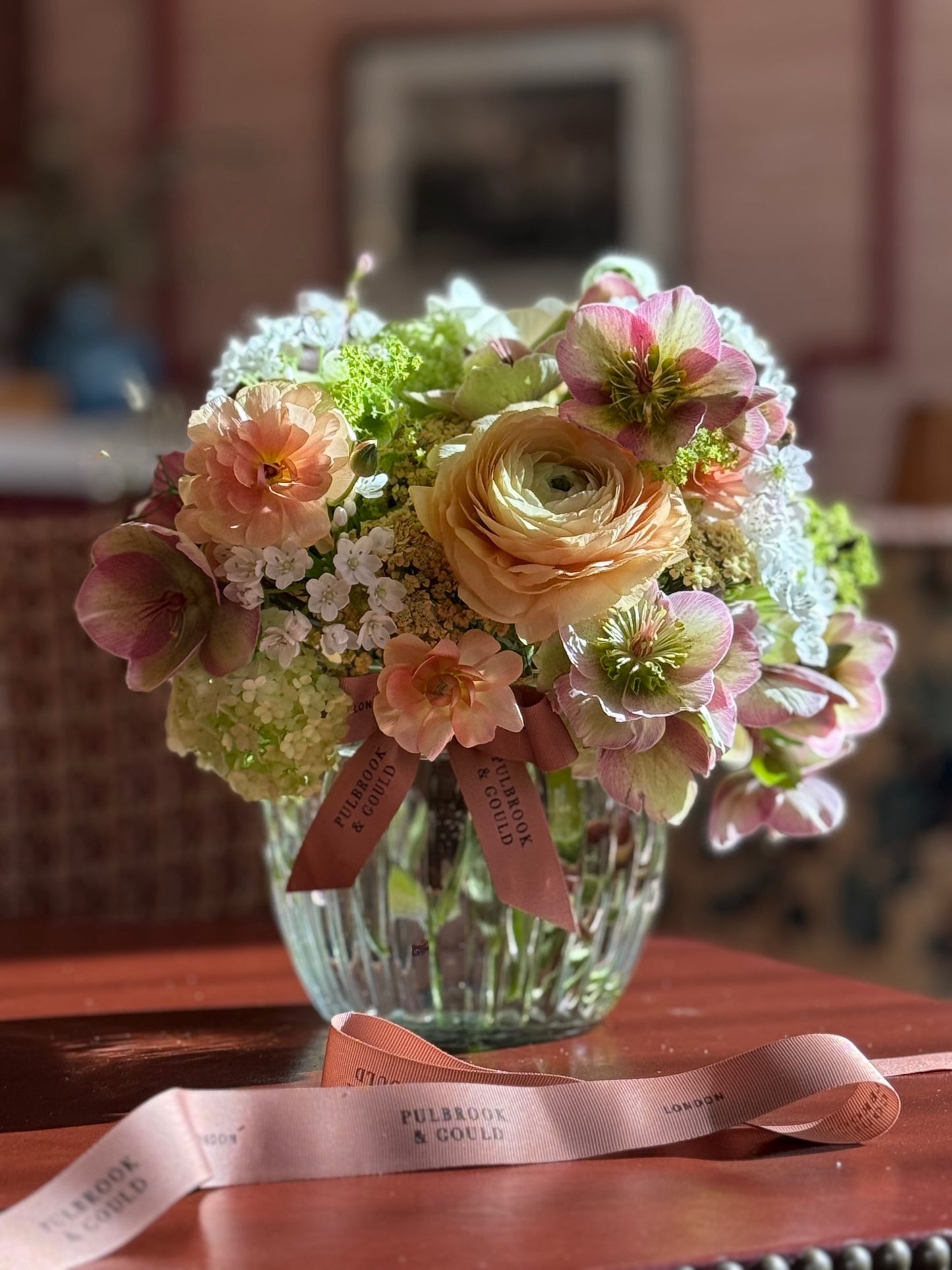 Bouquet of flowers in a clear vase with a pink ribbon on a wooden surface.