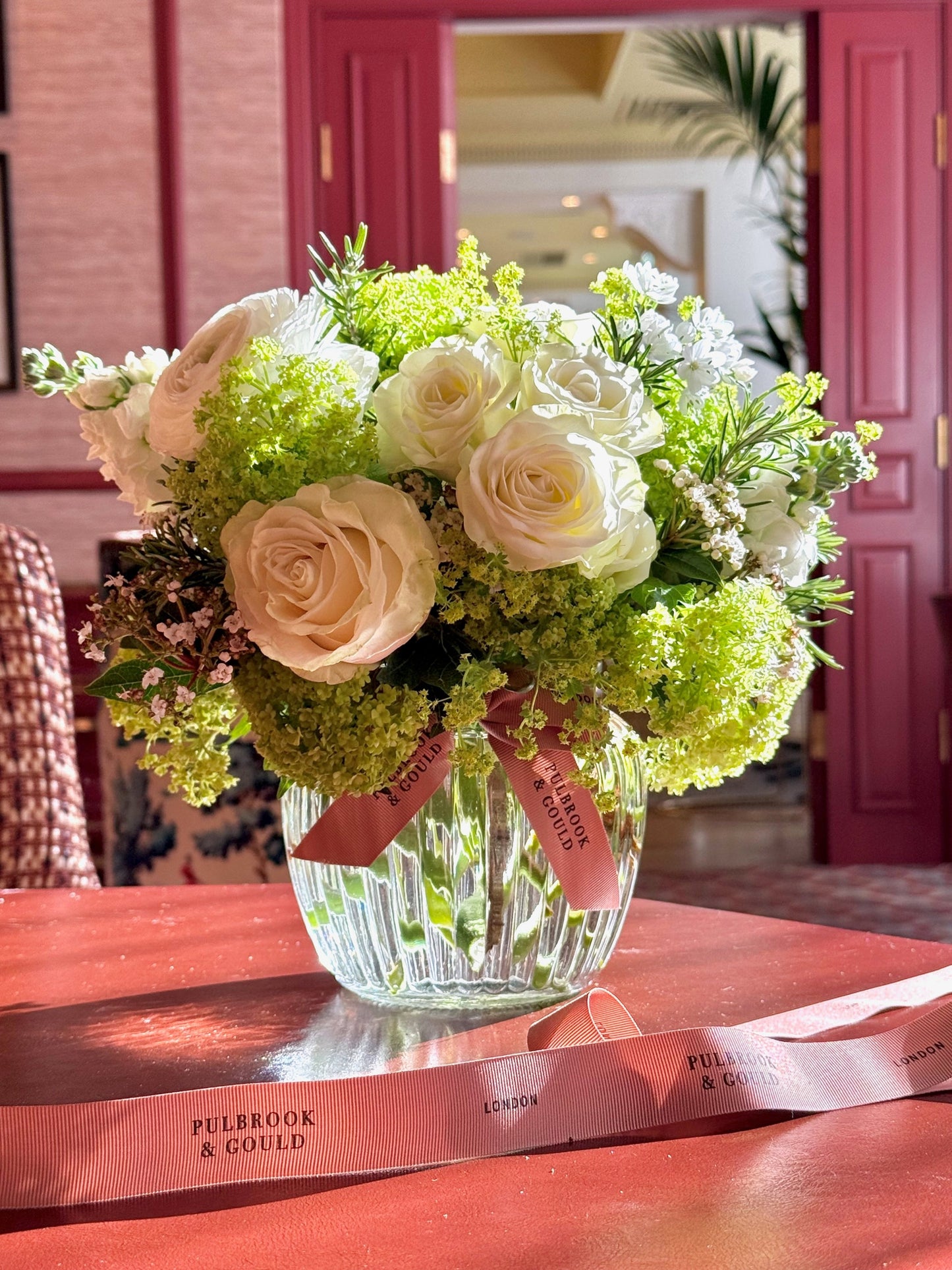 Bouquet of flowers in a clear vase on a red surface with a pink door in the background
