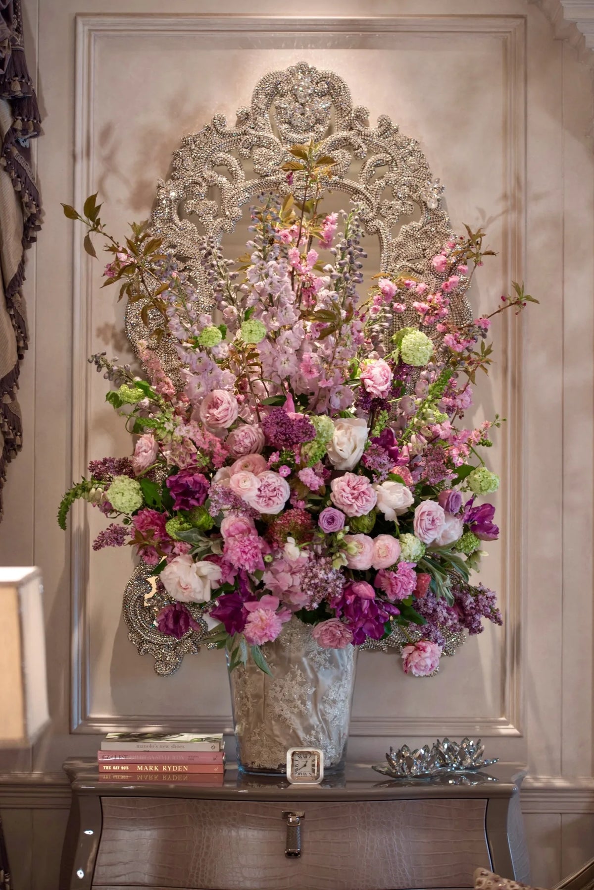 Large pink and purple weekly flower arrangement in a stone urn against an ornate mirrored console, by Pulbrook & Gould