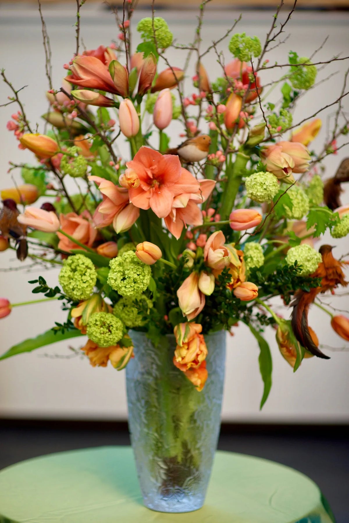 Coral amaryllis and tulip arrangement with viburnum in a glass vase, weekly flowers by Pulbrook & Gould, London