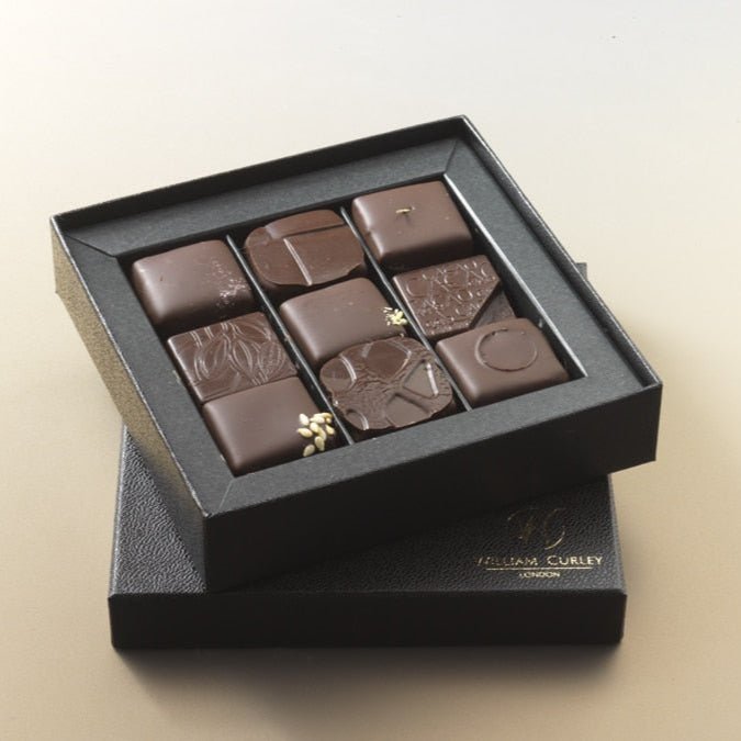 A box of William Curley handmade chocolates containing nine pieces, with each chocolate piece showcasing intricate designs on the top.