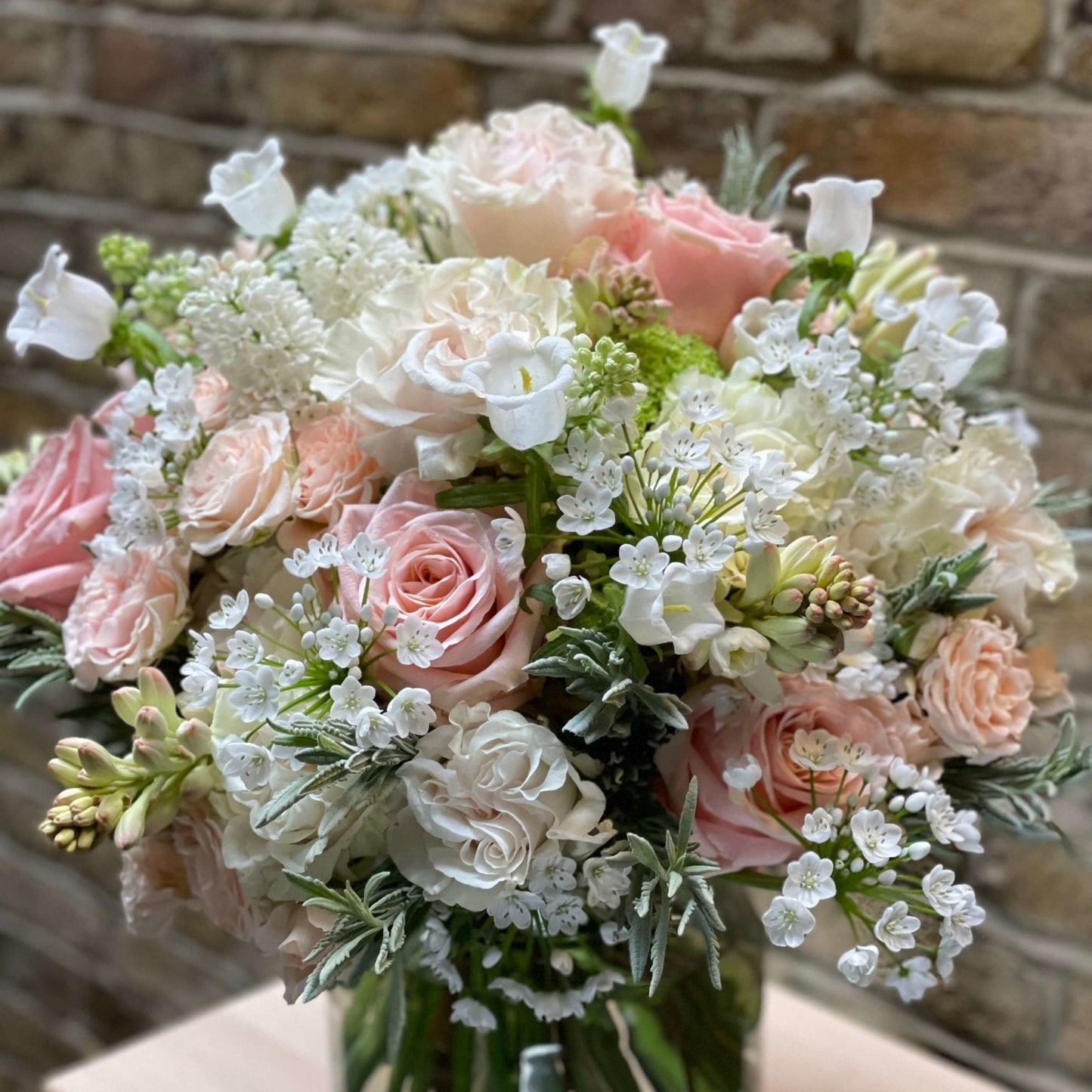 Bouquet of pink and white flowers in a vase against a brick wall.