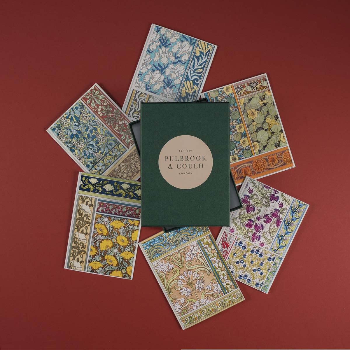 A collection of colorful botanical illustrated greetings cards from Tolstoy Gallery, displayed neatly with their envelopes on a red background.